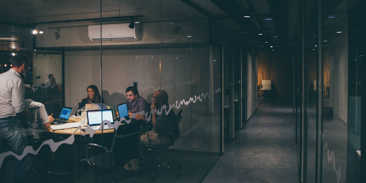Oficina acristalada en penumbra con varias personas trabajando frente a sus portátiles