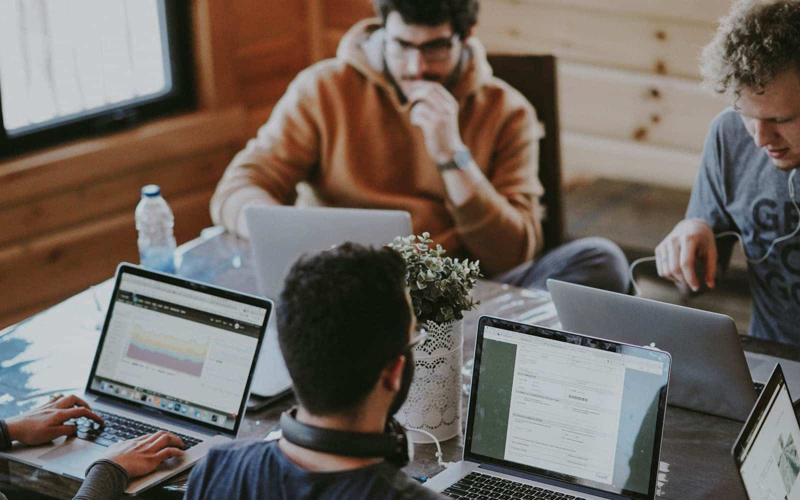 Equipo de trabajo con varios portátiles alrededor de una mesa en una oficina luminosa