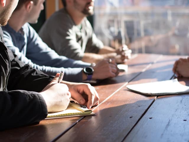 Asistentes tomando notas alrededor de una mesa larga en una sesión de trabajo