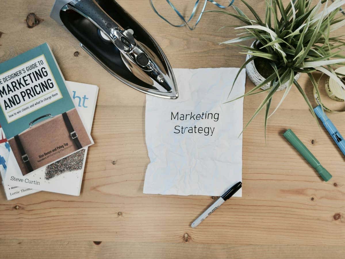 Cuaderno con la anotación marketing strategy junto a libros y una planta sobre una mesa
